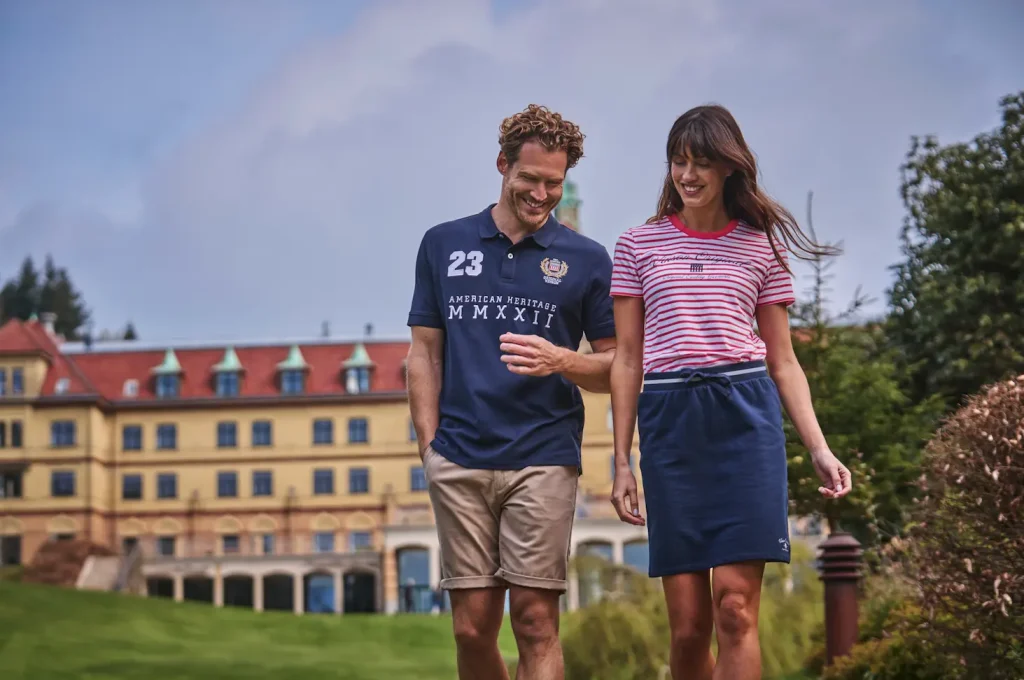 Hombre con polo azul marino y mujer con camiseta de rayas rojas y falda deportiva azul - Colección verano VINSON
