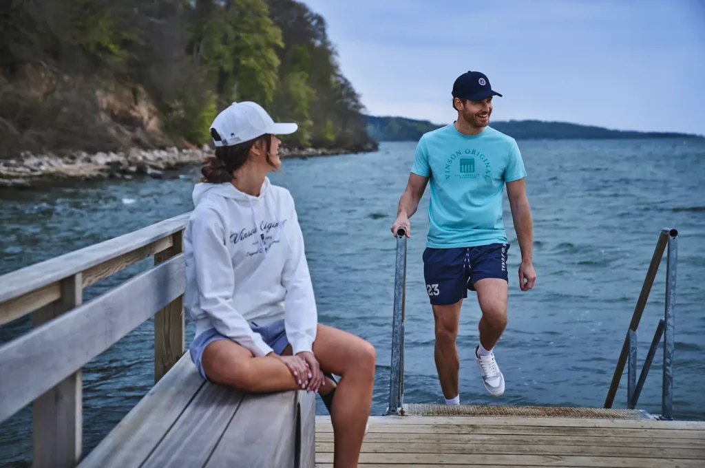 Mujer con sudadera blanca y pantalón corto deportivo y hombre con camiseta azul y pantalón azul marino corto deportivo - Colección verano VINSON