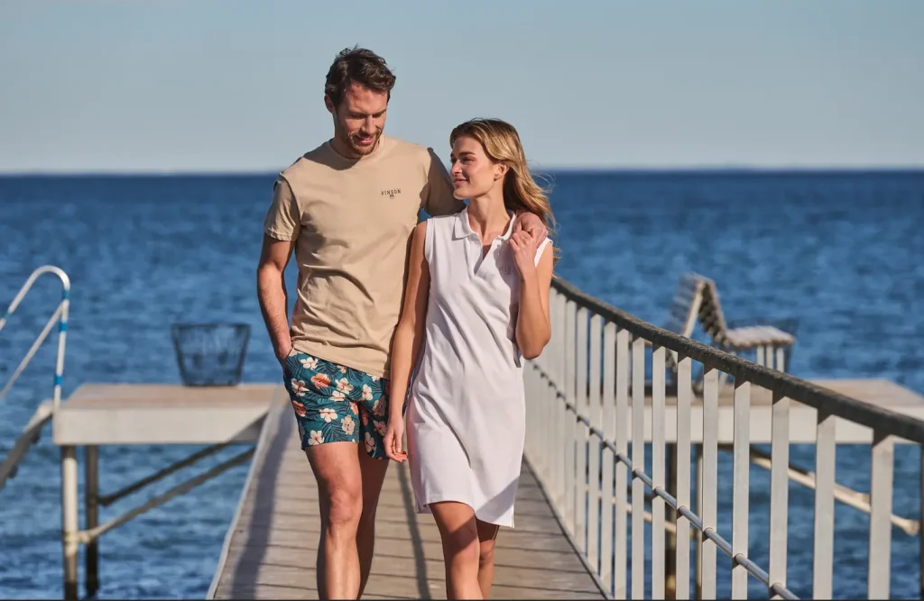 Hombre con camiseta y bañador de flores y mujer con vestido polo blanco - Colección verano VINSON